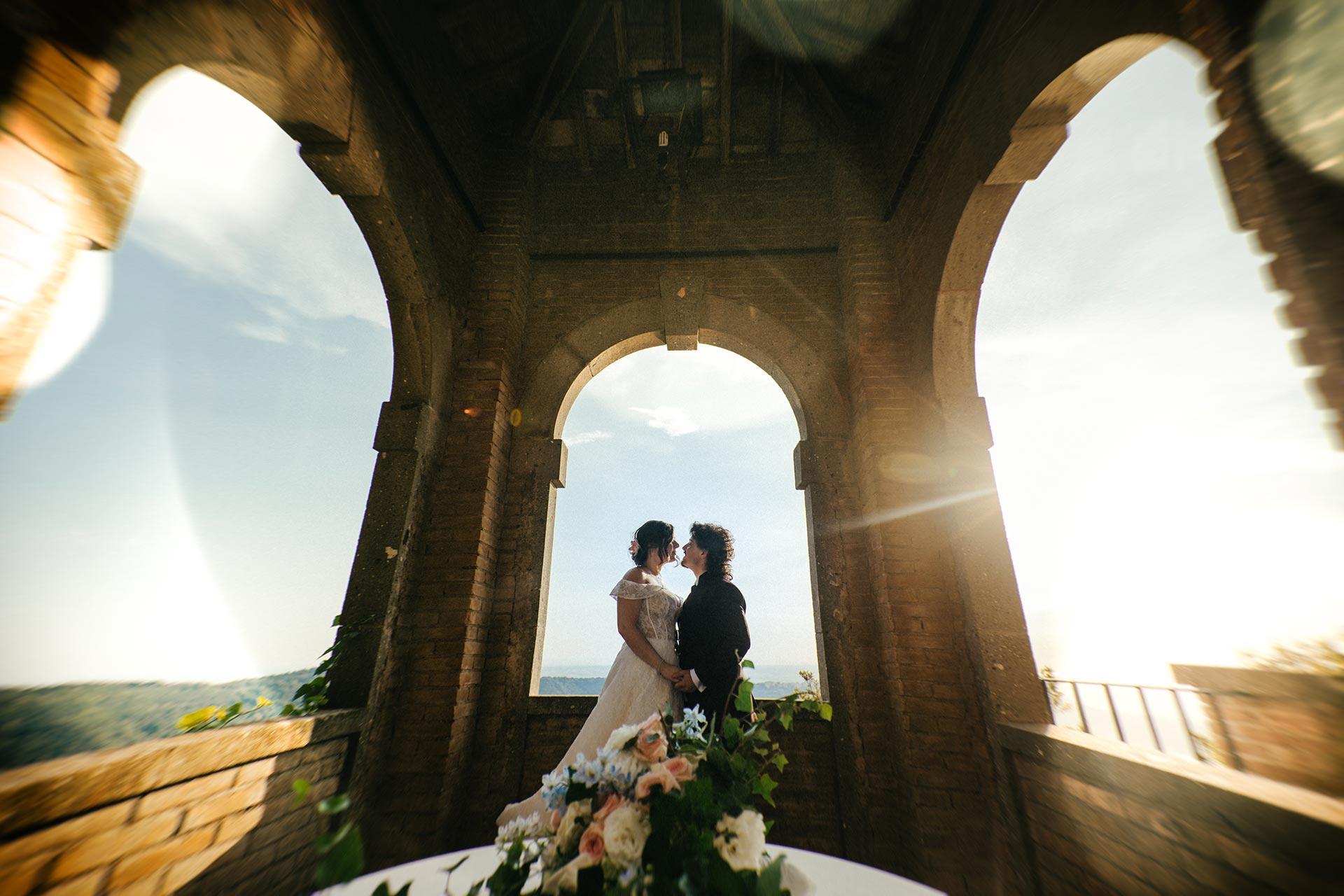 Fotografo matrimonio Villa del Cardinale Castelli Romani Sposi si baciano sotto un arco panoramico a Villa del Cardinale, Castelli Romani