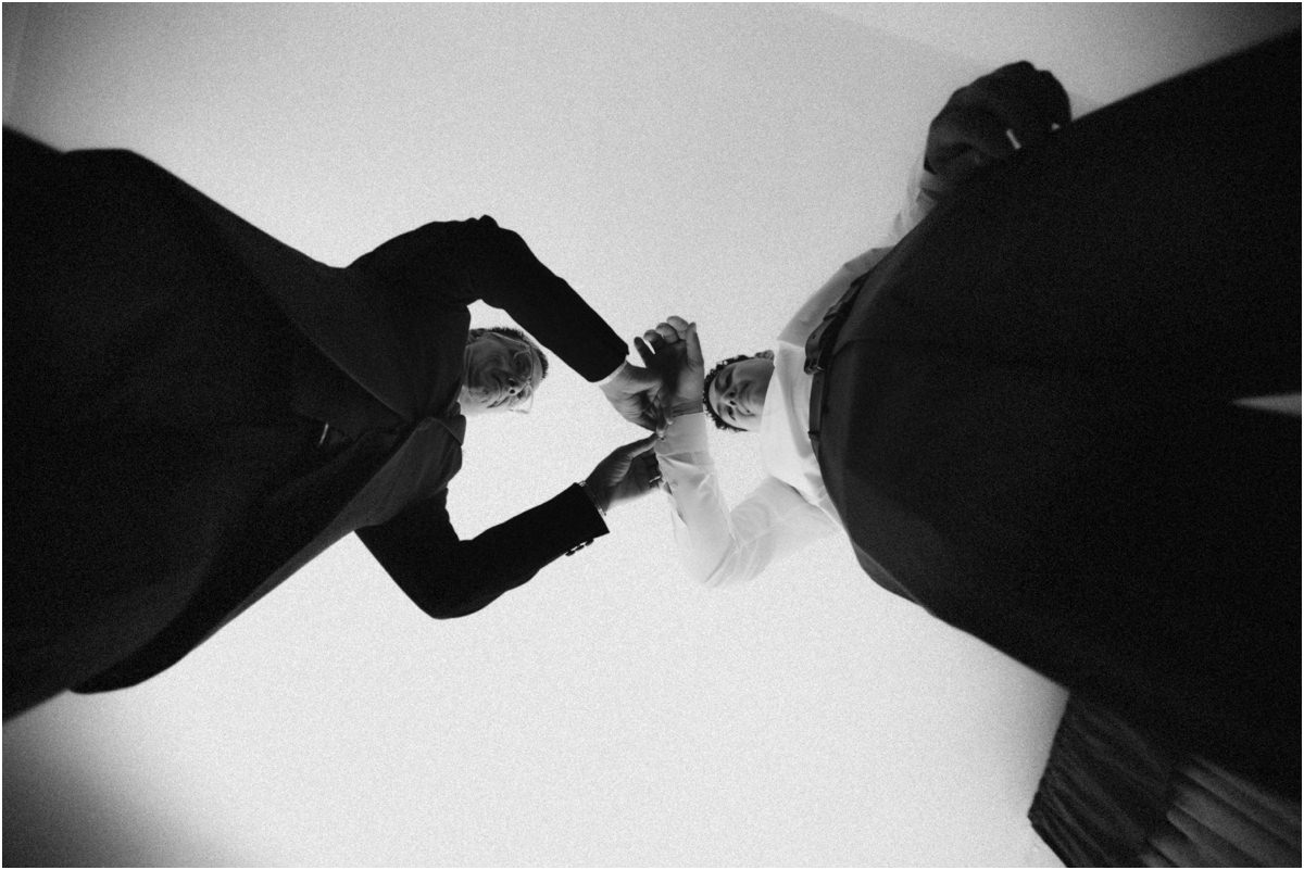 Foto in bianco e nero dal basso dello sposo aiutato con i polsini della camicia