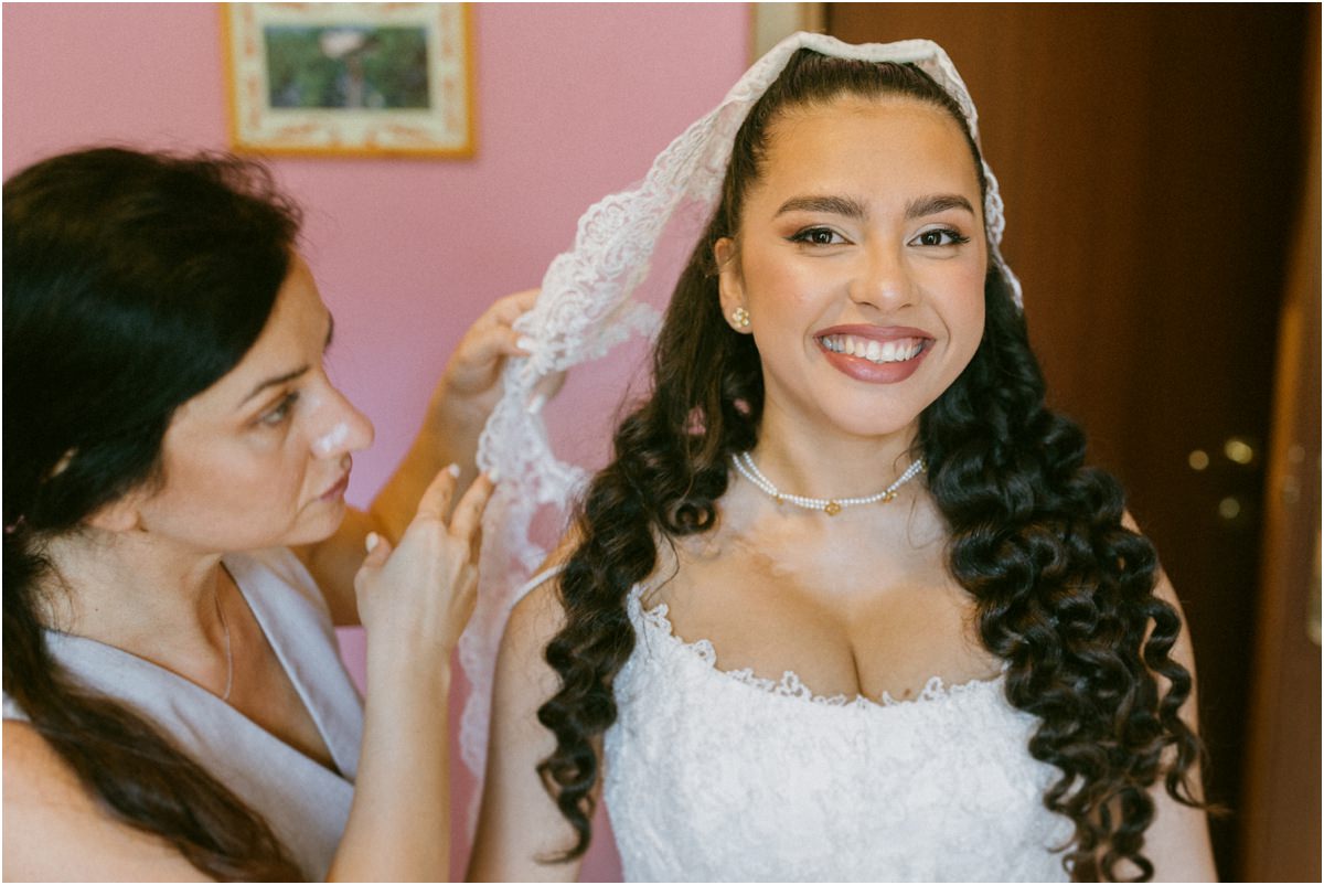 Sorriso della sposa mentre le sistemano il velo di pizzo
