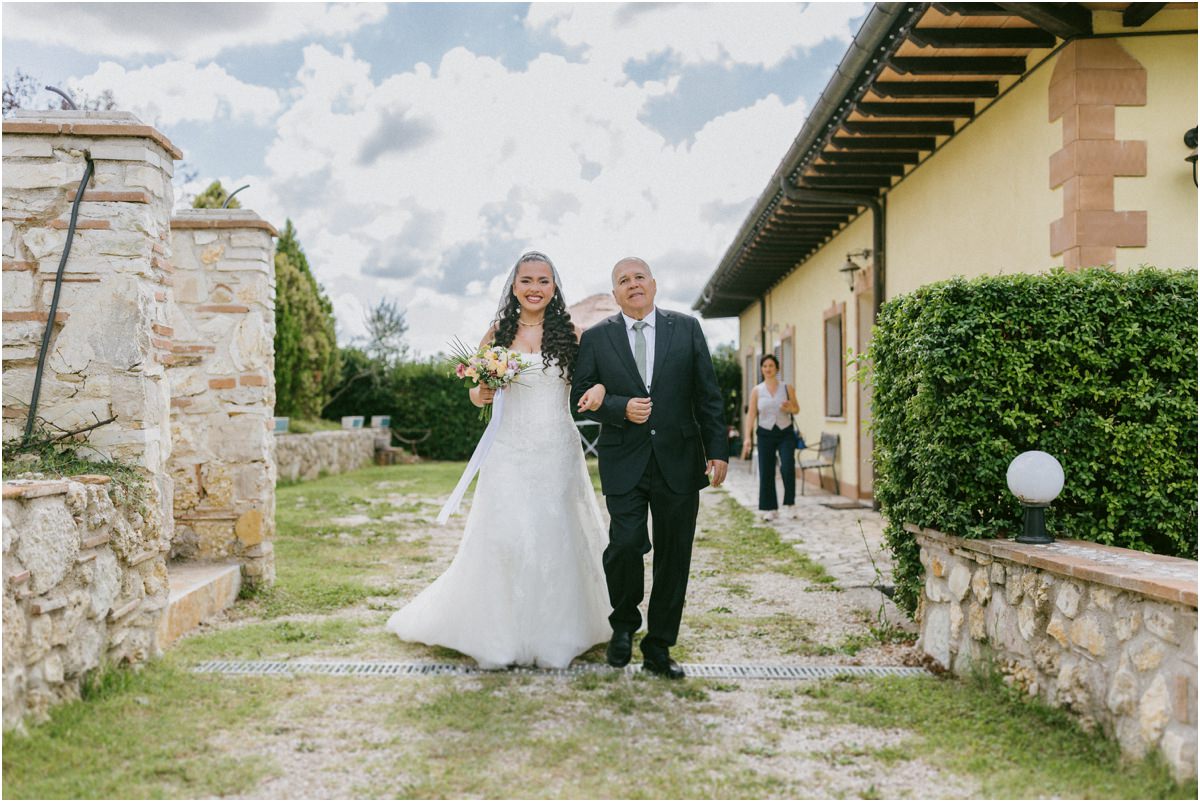 La sposa con il bouquet cammina con il papà verso il rito all'aperto in Sabina