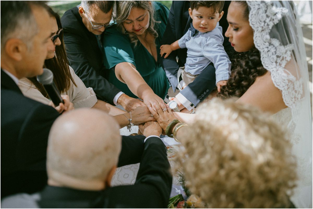Le mani unite di sposi, familiari e del figlio durante la benedizione del rito all'aperto