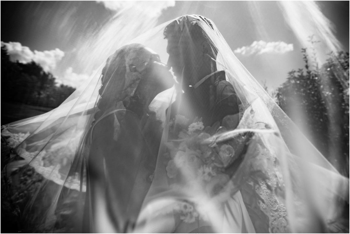 Foto in bianco e nero del bacio degli sposi sotto il velo in controluce