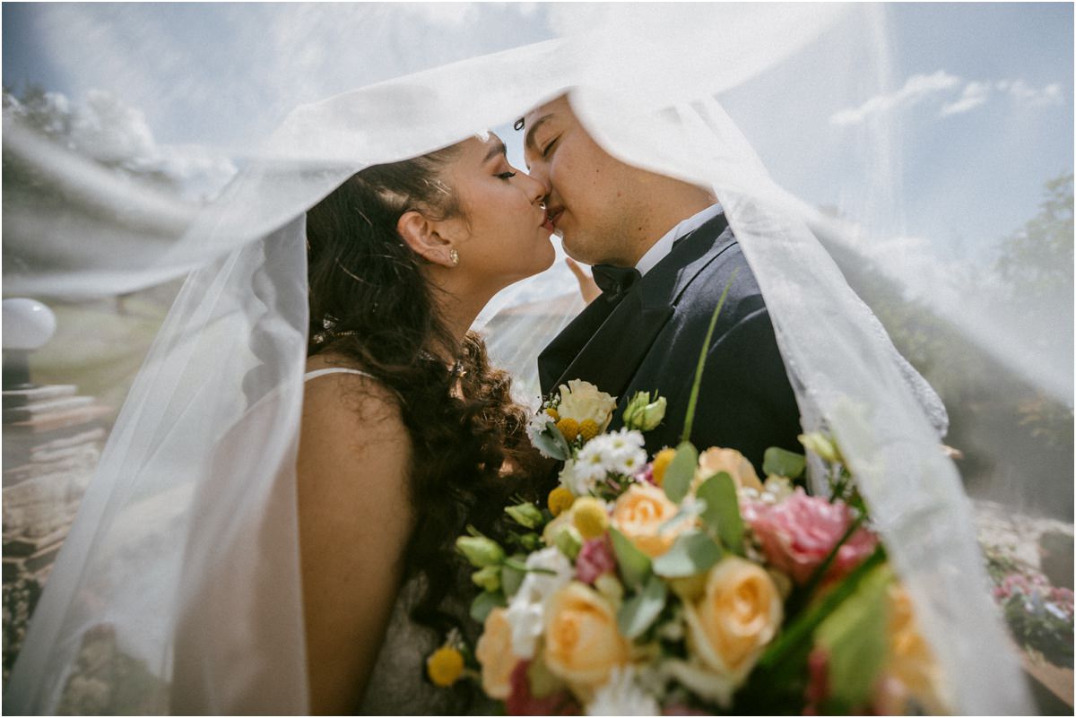 Bacio di Andrea e Orlando sotto il velo da sposa con il bouquet in primo piano