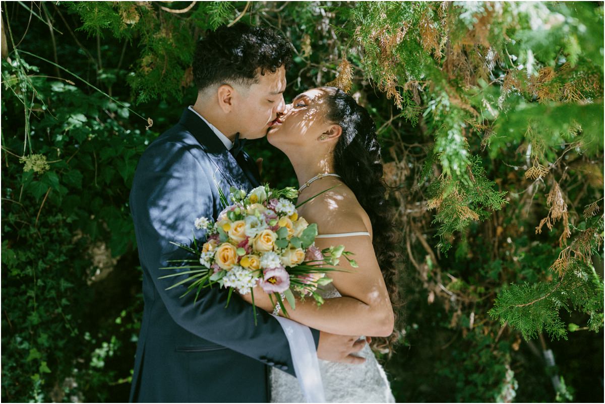 Bacio degli sposi tra il verde della tenuta con il bouquet colorato in mano