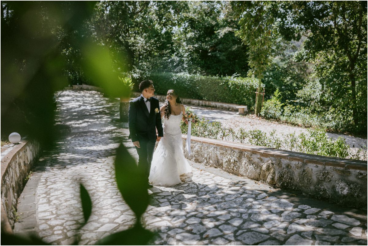 Andrea e Orlando camminano abbracciati sul sentiero di pietra del giardino verso la festa