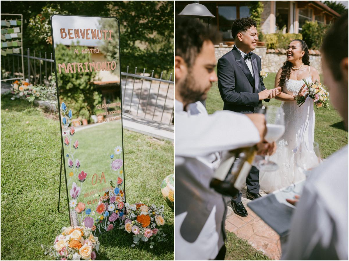 Cartello di benvenuto al matrimonio con fiori dipinti e brindisi degli sposi nel giardino della tenuta
