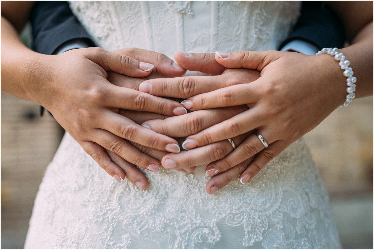 Le mani degli sposi intrecciate con le fedi sull'abito di pizzo della sposa