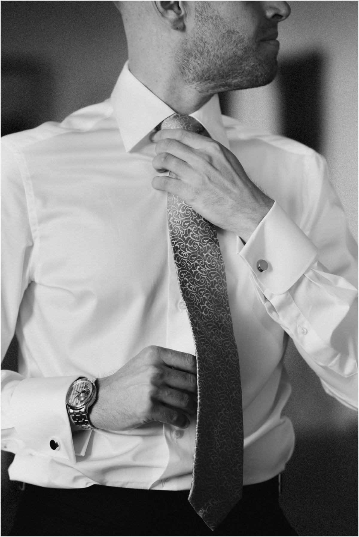 Groom Adjusting His Tie, Black and White Black and white detail of groom Angus adjusting his patterned tie, with watch and cufflinks