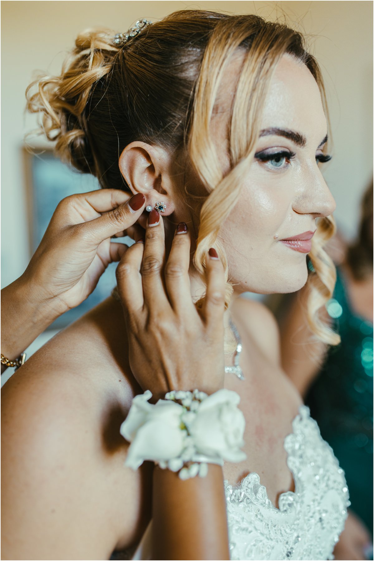 Bride Earring Detail Close-up of a bridesmaid with a white rose wrist corsage putting an earring on bride Miriana