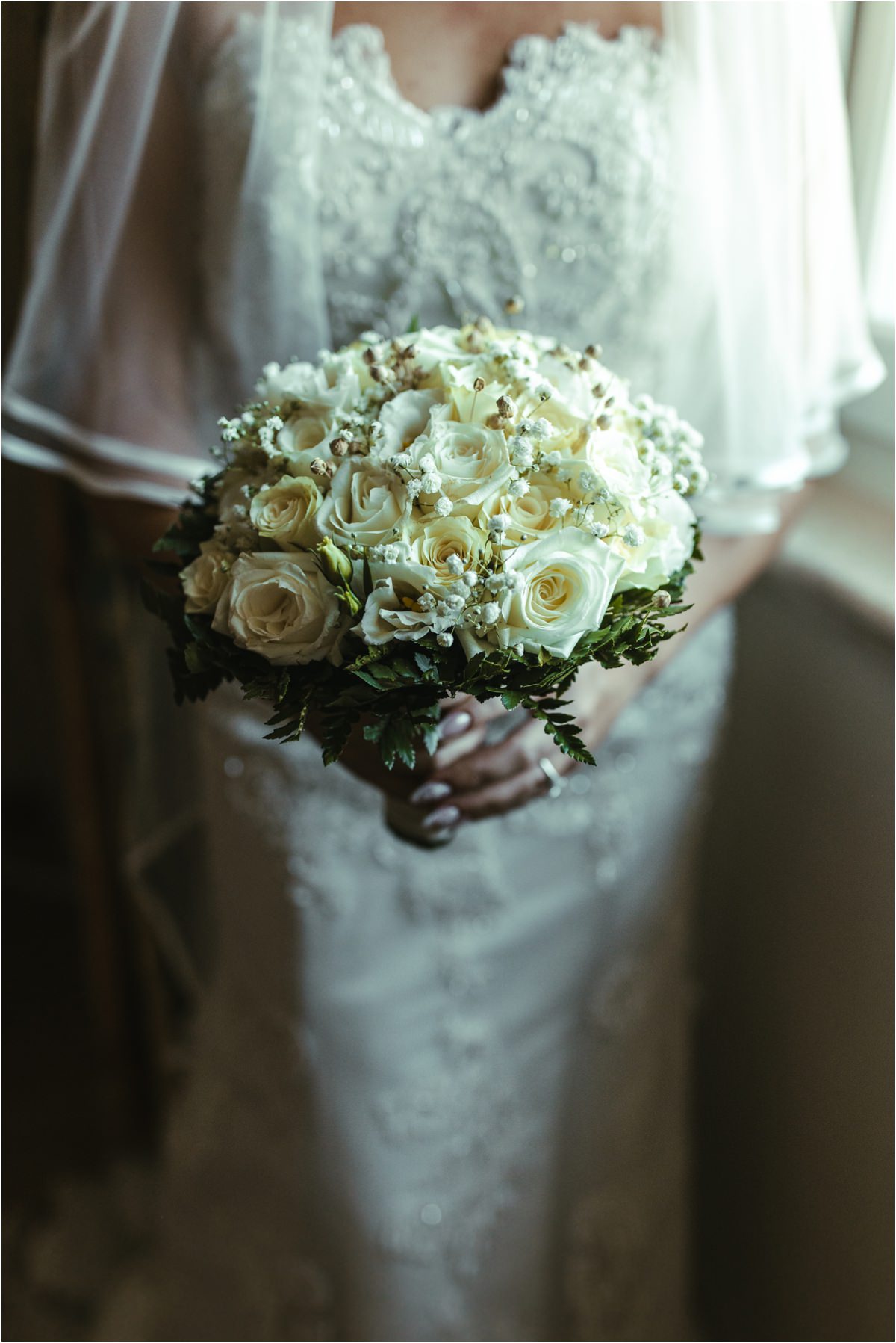 White Roses Bridal Bouquet Detail of the bridal bouquet of white roses and baby breath held by Miriana against her lace dress