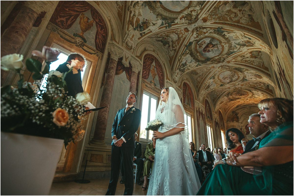 Bride and Groom at the Ceremony Table Miriana and Angus standing in front of the officiant with flowers and frescoes of the Pannini Gallery around them