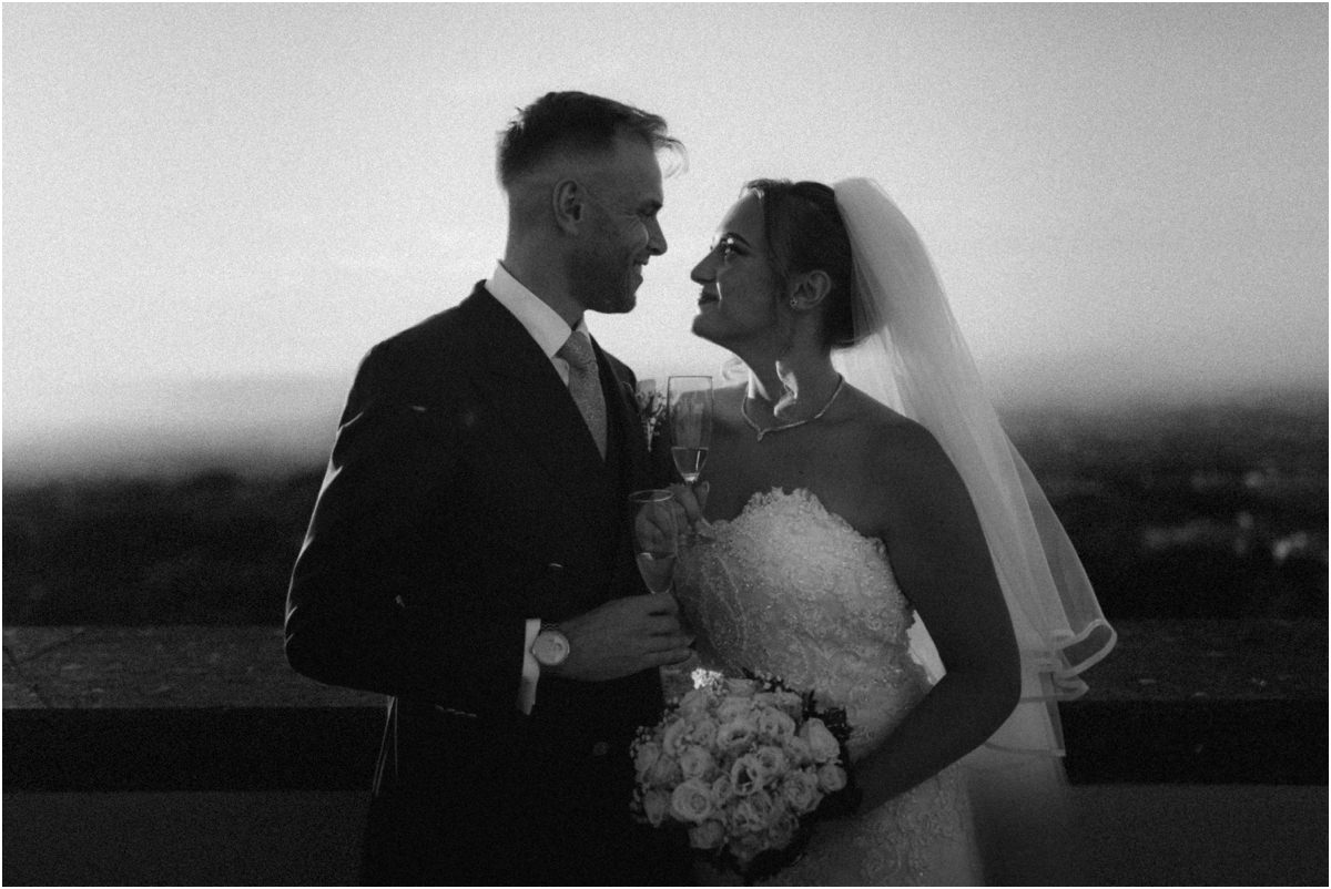 Newlyweds Face to Face, Black and White Black and white photo of Miriana and Angus smiling face to face with champagne and bouquet on the terrace
