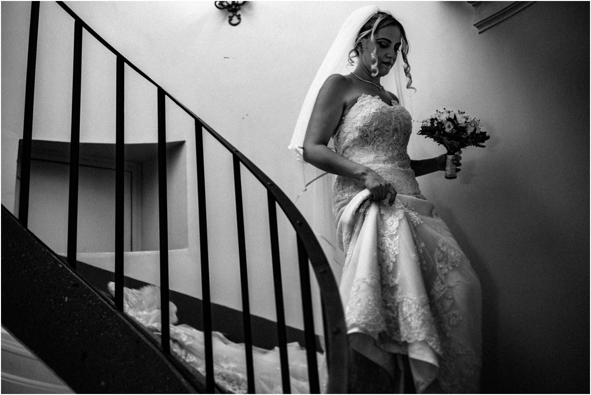 Bride on the Staircase, Black and White Black and white photo of bride Miriana walking down a curved staircase holding her dress and bouquet