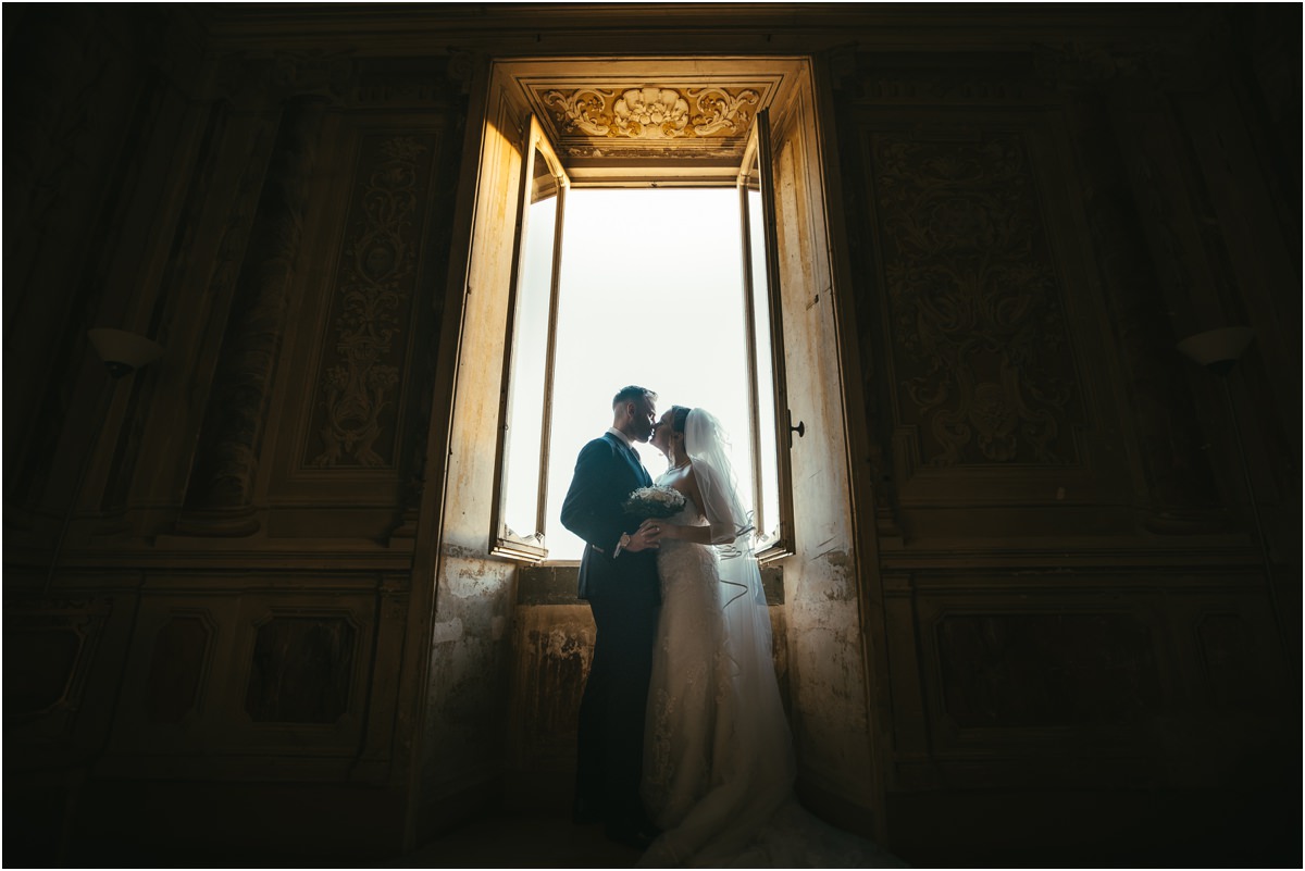 Newlyweds in a Frescoed Window of Villa Grazioli Miriana and Angus embracing in the light of a tall window in a dark frescoed room of Villa Grazioli
