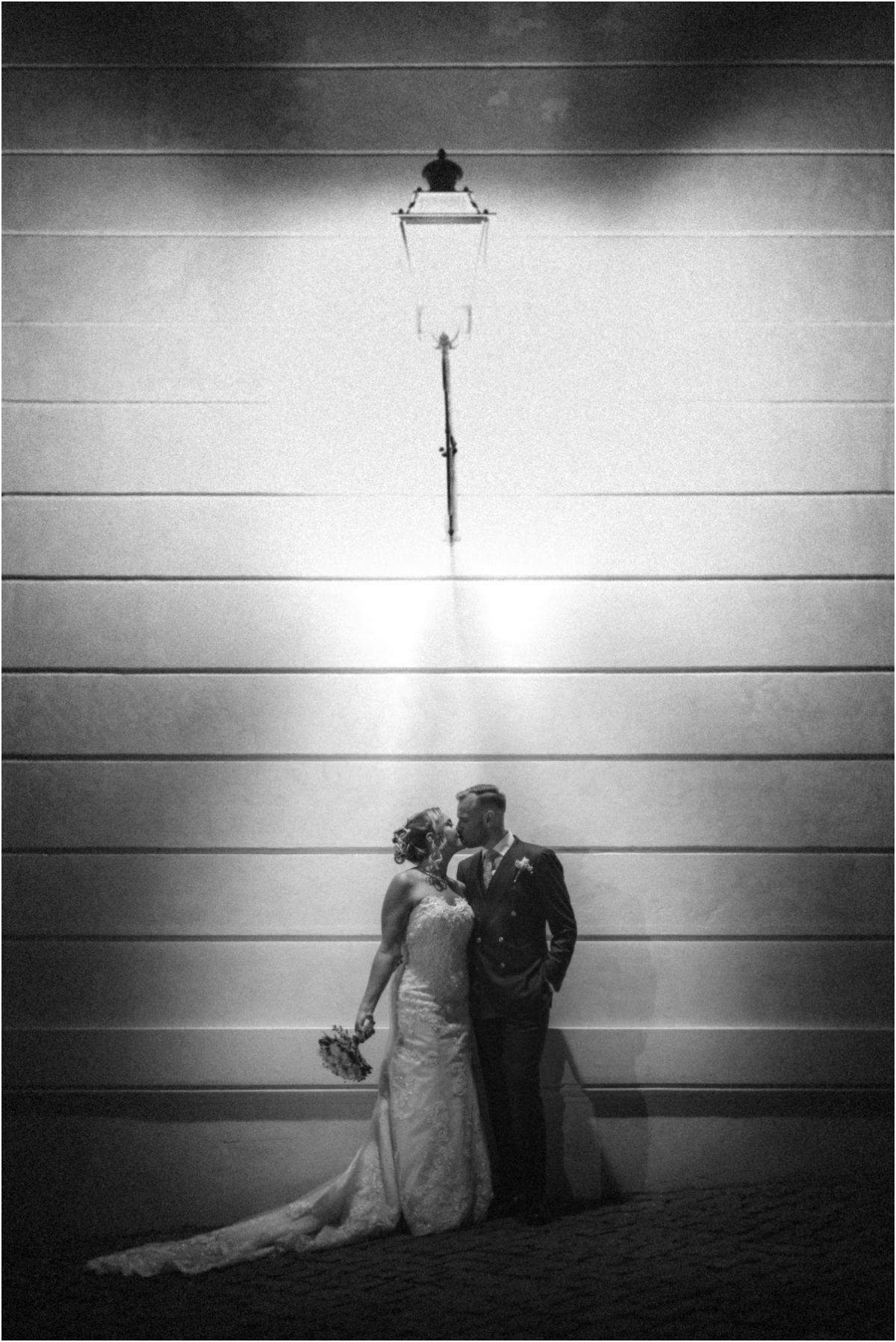 Kiss Under the Lantern, Black and White Black and white photo of Miriana and Angus kissing under a wall lantern at Villa Grazioli