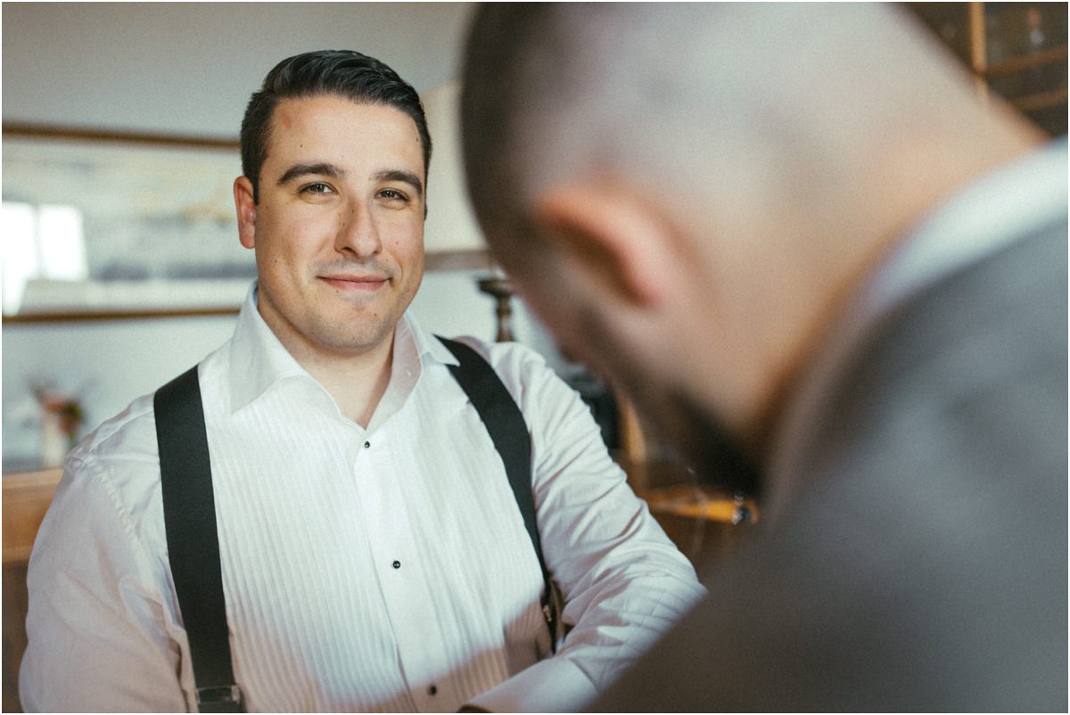Alessio Smiling While Getting Ready Groom Alessio smiling in white shirt and black braces while a guest helps him get ready at Villa Grazioli