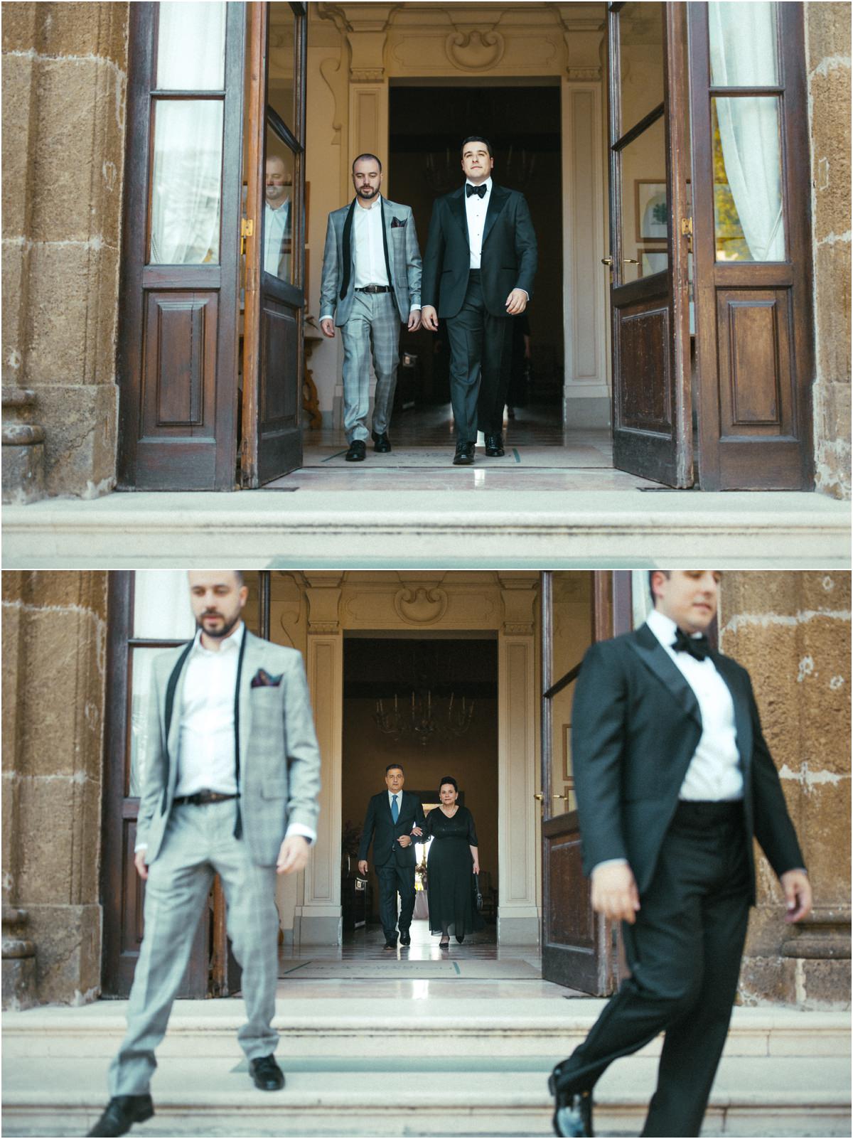 Groom Walking Out of Villa Grazioli Groom Alessio and a guest in a grey suit walking down the steps of Villa Grazioli, family behind them