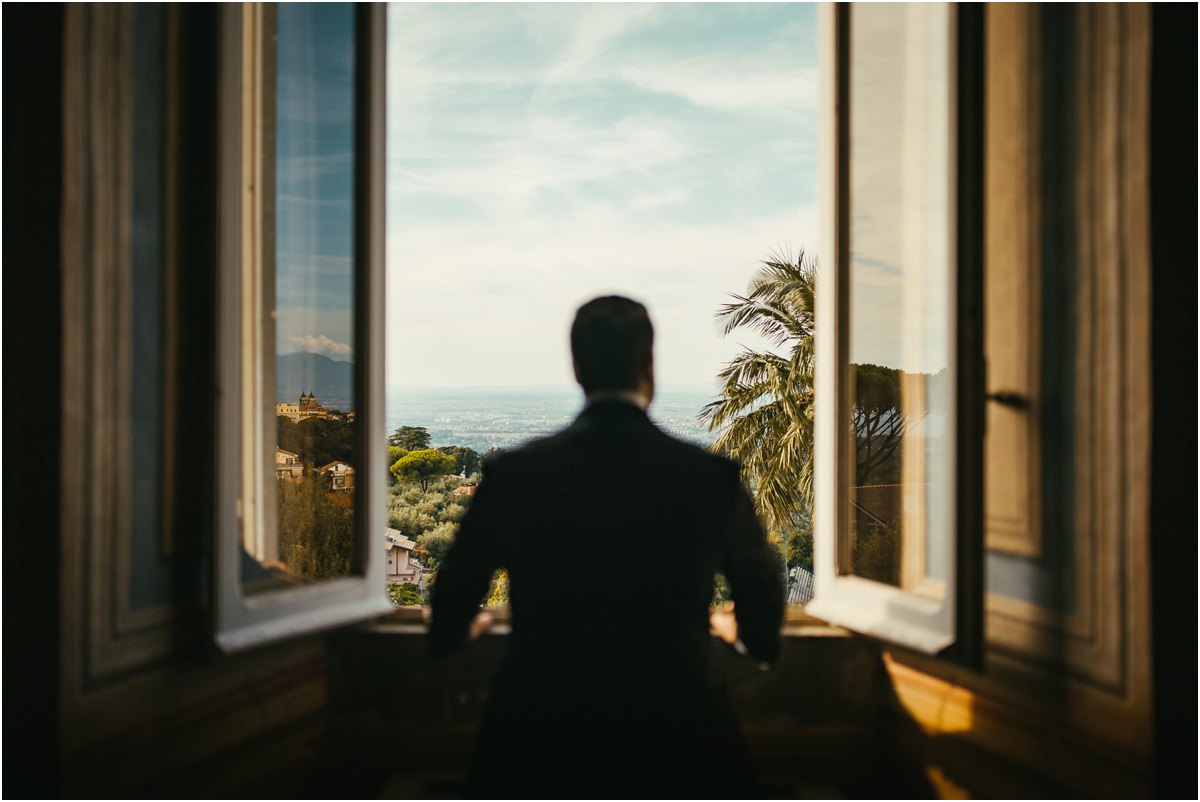 Looking Out of the Window Groom Alessio seen from behind at an open window of Villa Grazioli, looking at the view on a sunny morning