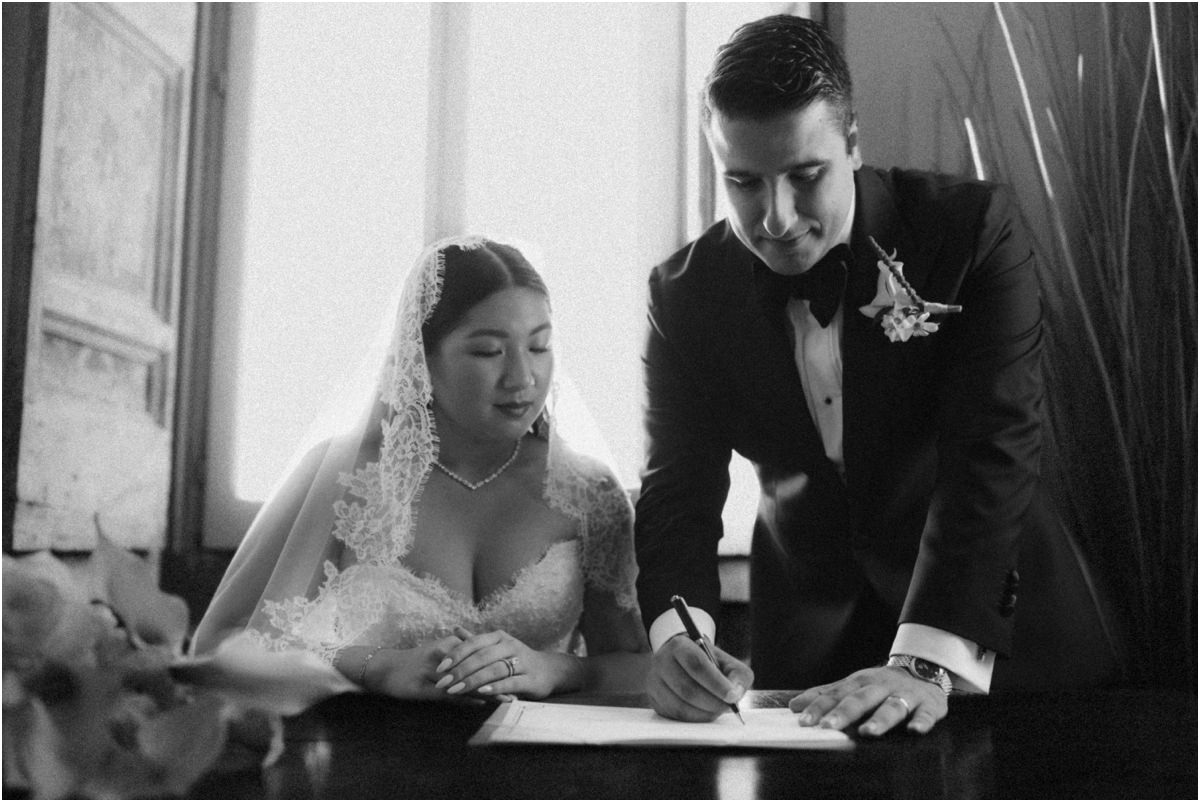 Signing the Register Black and white photo of groom Alessio signing the marriage register next to bride Leah