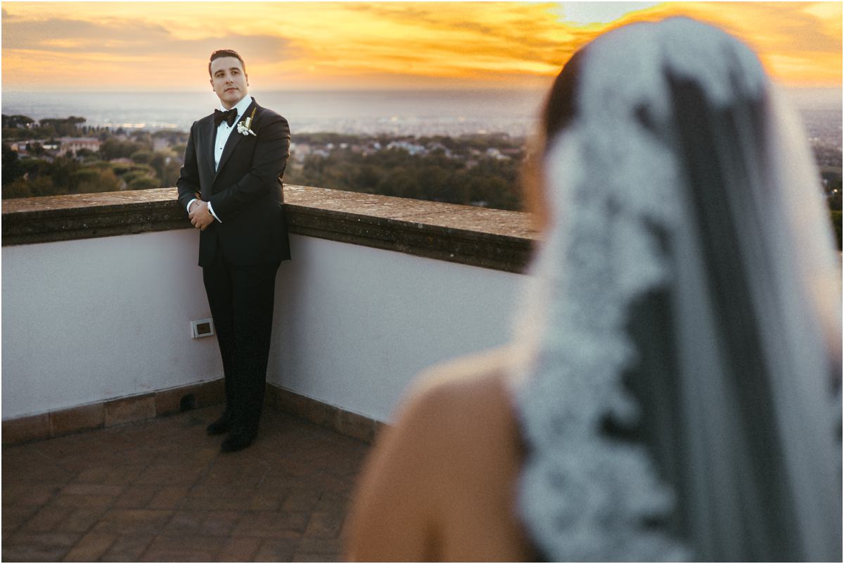 Alessio Waiting on the Terrace Groom Alessio standing on the terrace of Villa Grazioli at sunset, Leah's lace veil blurred in the foreground