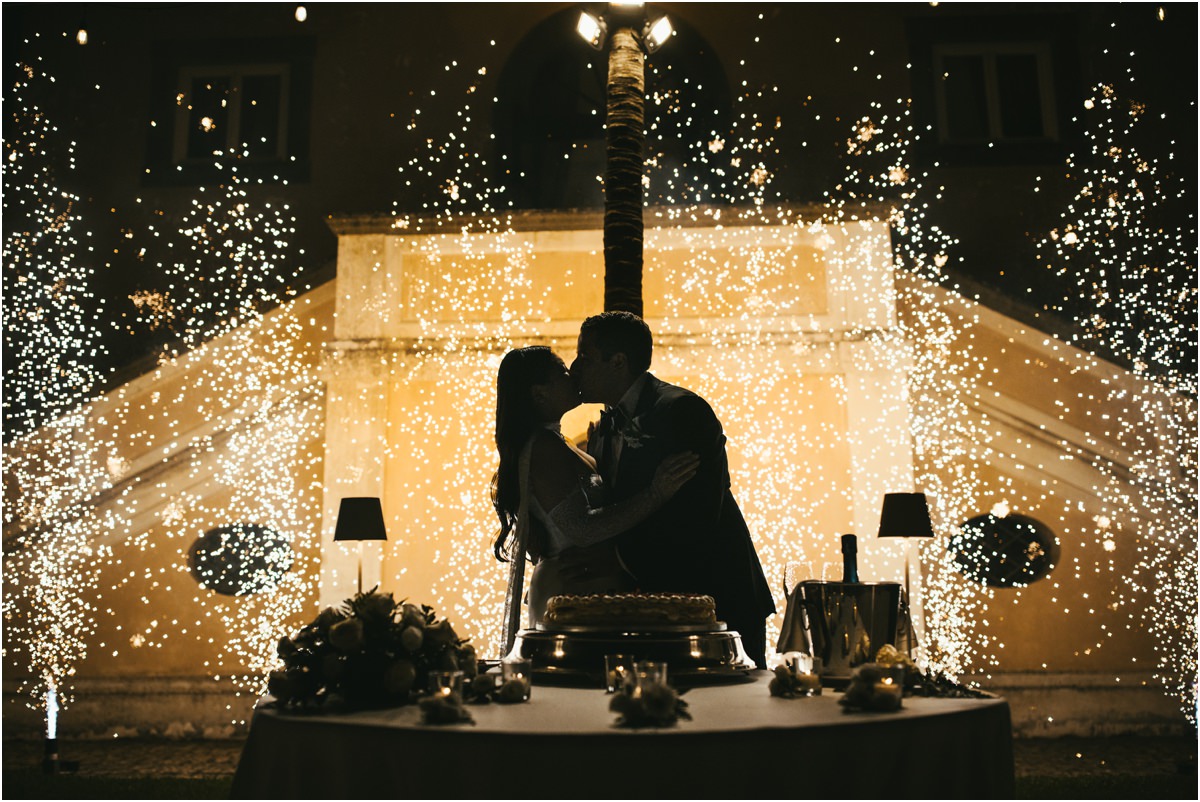 Cake Cutting with Sparklers Alessio and Leah kissing behind the wedding cake between cold sparklers at night