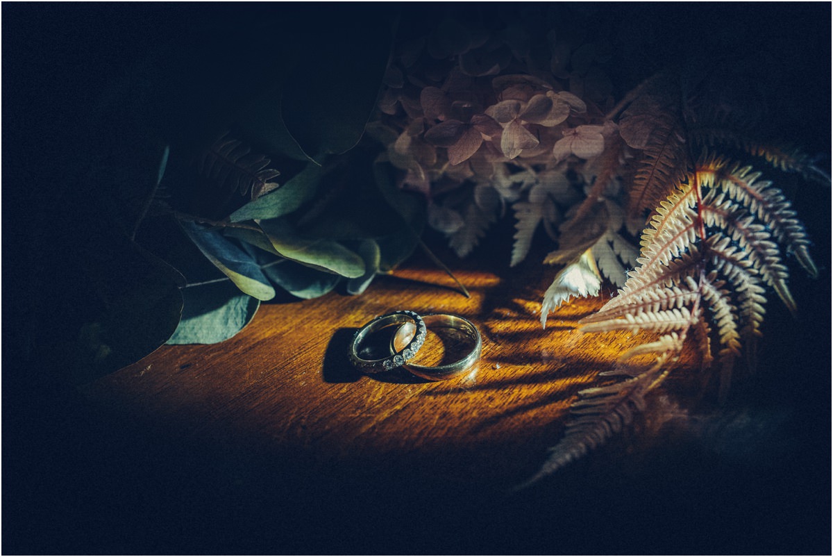 The Wedding Rings Alessio and Leah's wedding rings on a wooden table with leaves and fern at night