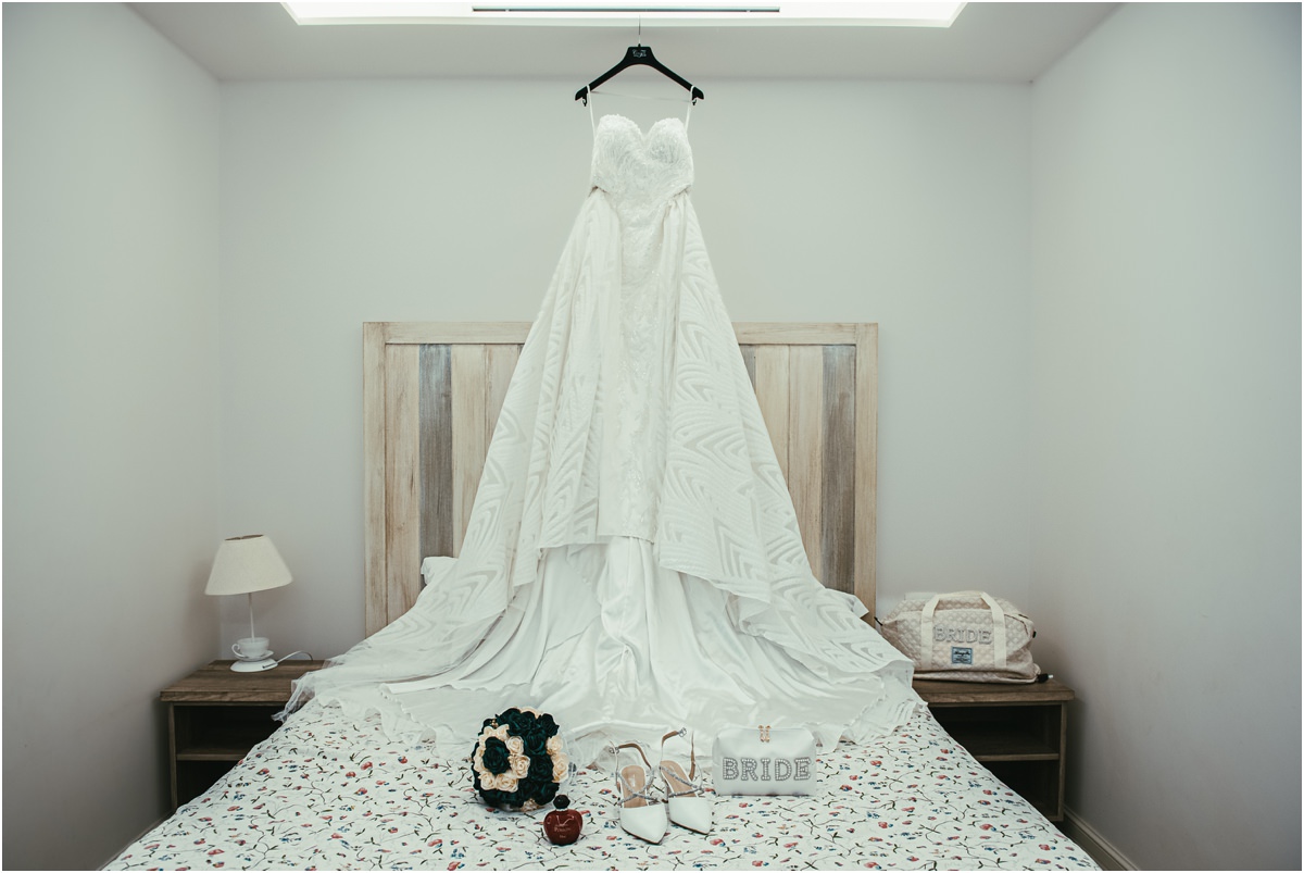 L'abito di Martina Abito da sposa di Martina appeso sopra il letto, con bouquet verde e bianco e scarpe da sposa a Le Jardin Potager