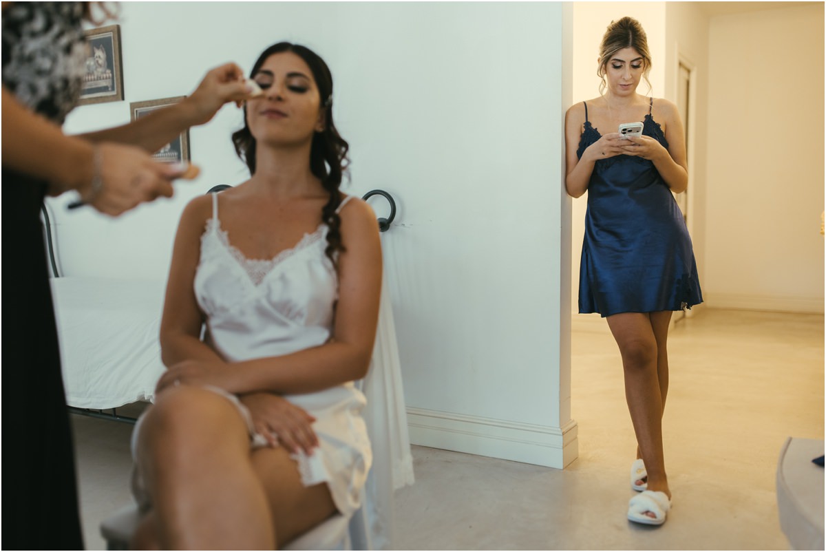 Un'amica di passaggio Martina durante il trucco mentre un'amica in vestaglia blu passa guardando il telefono