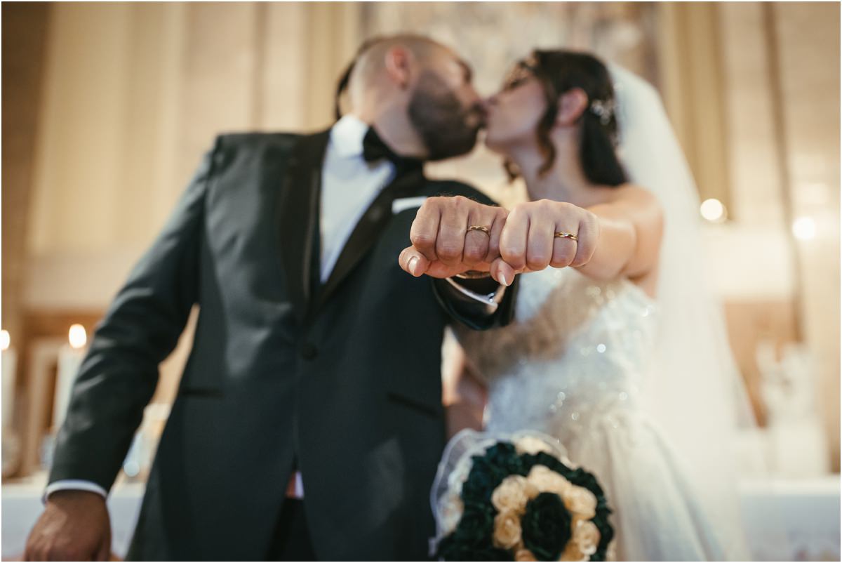 Le fedi Martina e Davide si baciano mostrando le fedi all'obiettivo, con il bouquet in primo piano