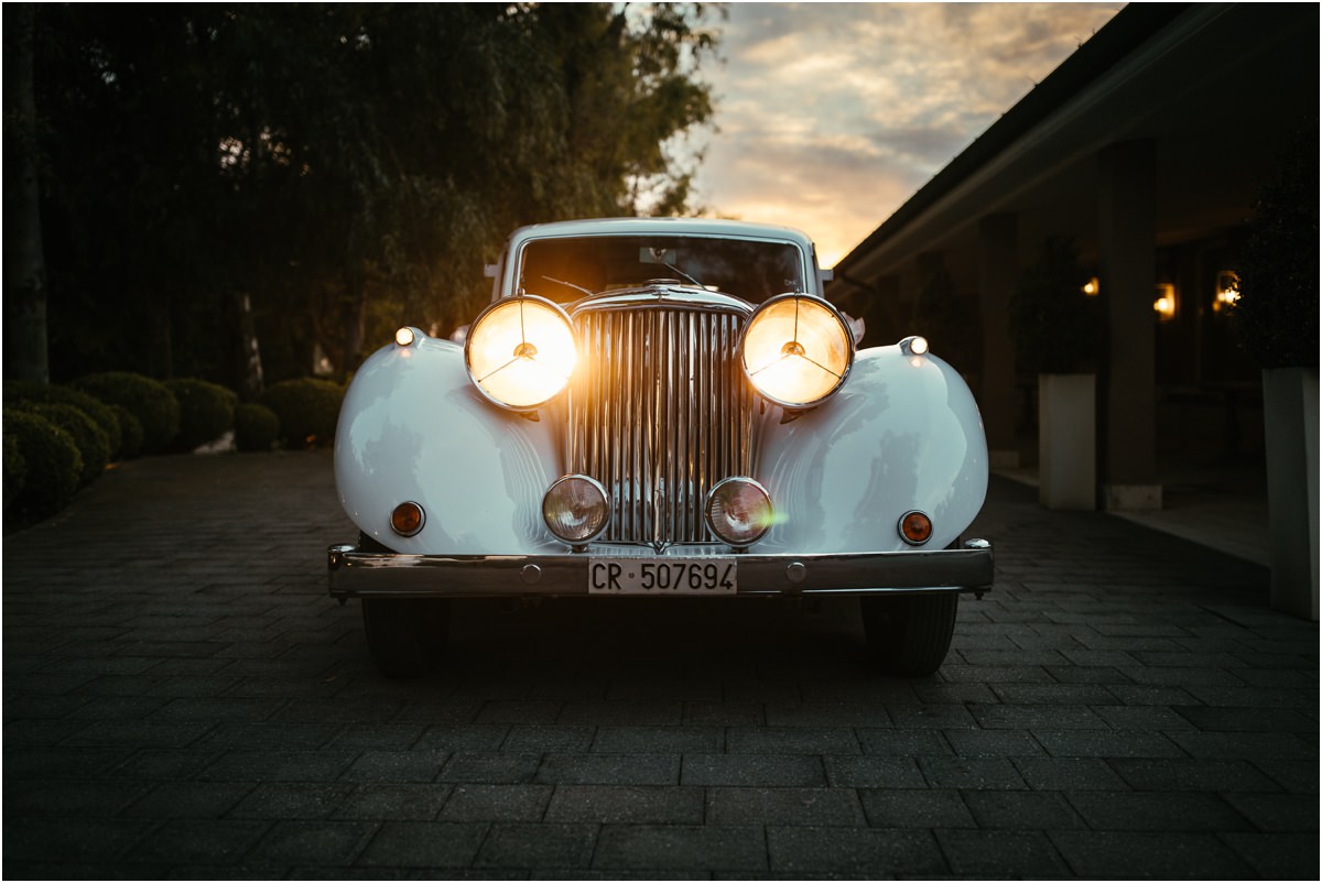 L'auto d'epoca al tramonto Fari accesi dell'auto d'epoca bianca degli sposi nel viale di Le Jardin Potager al tramonto