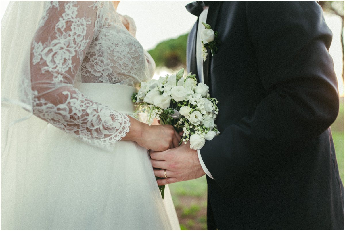 Bouquet e mani degli sposi Dettaglio delle mani degli sposi, del bouquet bianco e del pizzo dell'abito da sposa